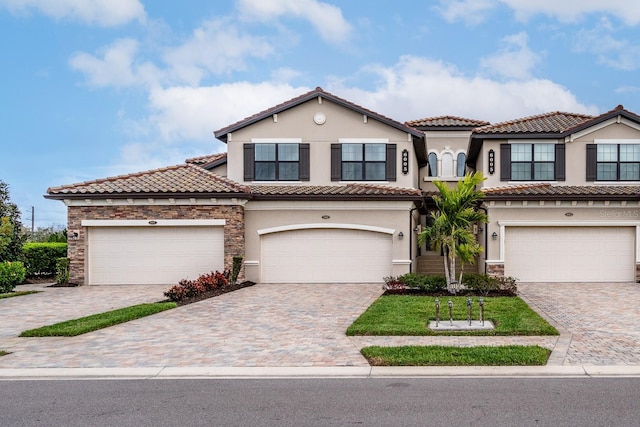 mediterranean / spanish home with an attached garage, stone siding, a tiled roof, decorative driveway, and stucco siding