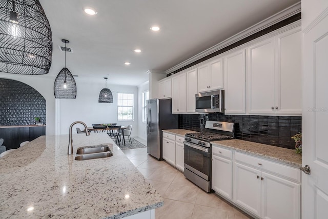 kitchen with appliances with stainless steel finishes, a sink, decorative light fixtures, and white cabinetry