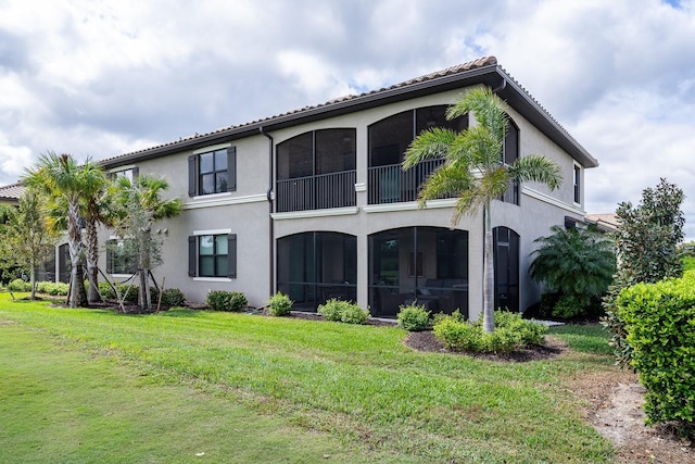 rear view of property featuring stucco siding, a sunroom, and a yard