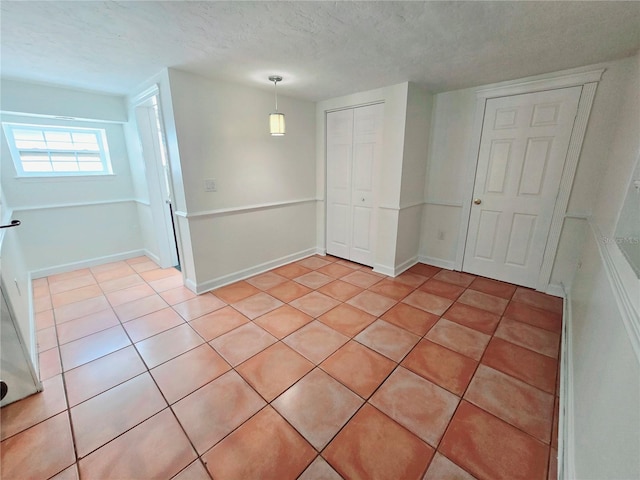 spare room with light tile patterned flooring, a textured ceiling, and baseboards