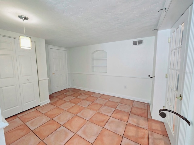 empty room with a textured ceiling, built in shelves, light tile patterned floors, and visible vents