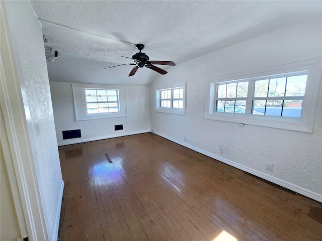 spare room featuring dark wood-type flooring, a textured wall, vaulted ceiling, and baseboards