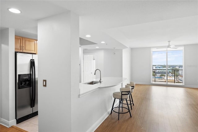 kitchen with light wood finished floors, a breakfast bar area, recessed lighting, a sink, and stainless steel fridge