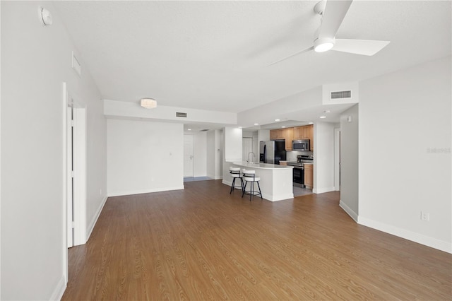 unfurnished living room featuring a ceiling fan, visible vents, baseboards, and wood finished floors