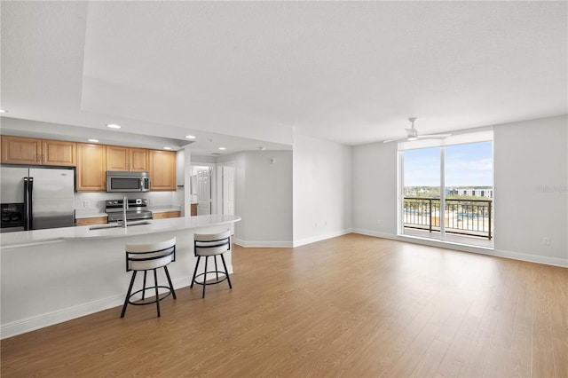 kitchen featuring light wood finished floors, appliances with stainless steel finishes, light countertops, a kitchen bar, and a sink