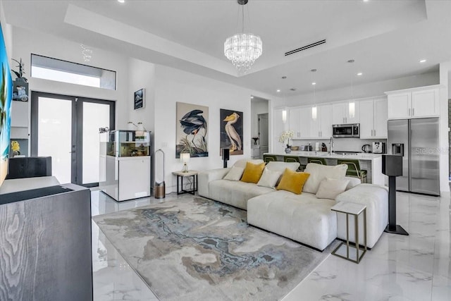 living area with marble finish floor, a raised ceiling, a notable chandelier, and french doors