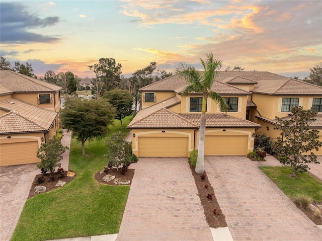 mediterranean / spanish-style house featuring decorative driveway, a tile roof, a lawn, and stucco siding