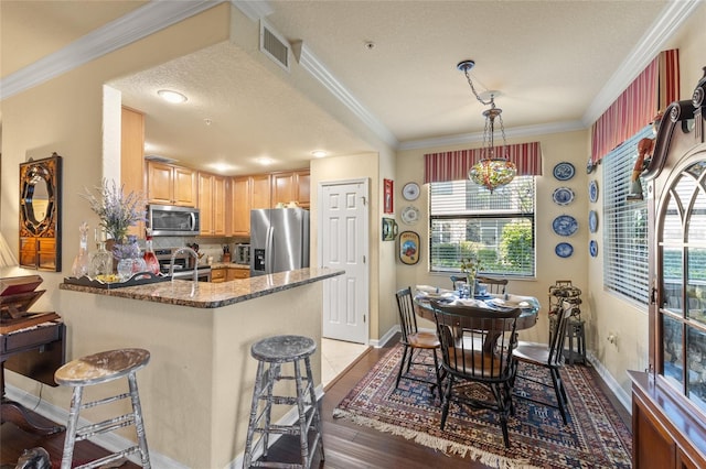 kitchen featuring visible vents, a peninsula, stainless steel appliances, crown molding, and light brown cabinetry