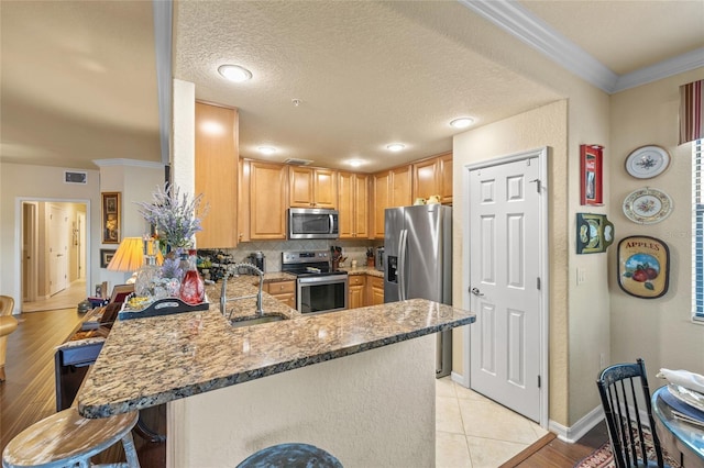 kitchen with a breakfast bar area, ornamental molding, a peninsula, stainless steel appliances, and a sink