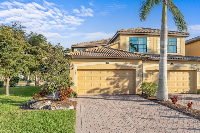 mediterranean / spanish home with a garage, a front lawn, decorative driveway, and stucco siding