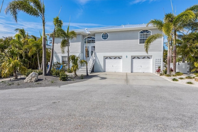 view of front facade featuring driveway, an attached garage, fence, french doors, and stucco siding