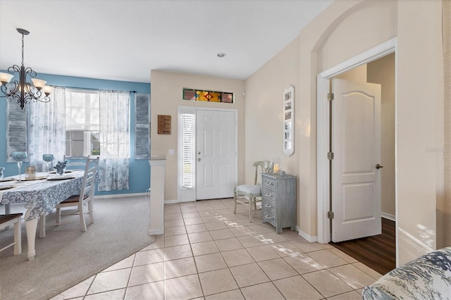 entrance foyer with light tile patterned flooring, a chandelier, light colored carpet, and baseboards