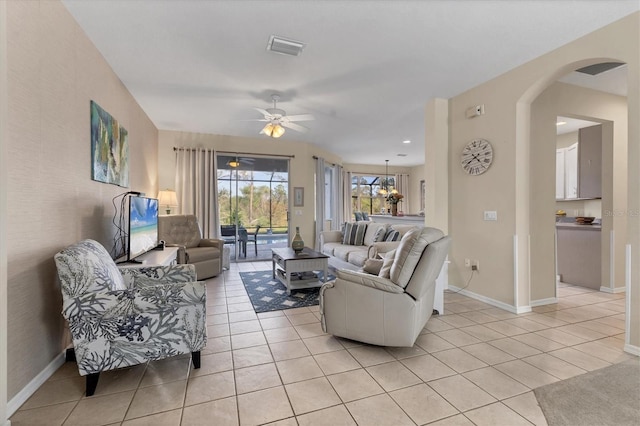 living room with visible vents, a ceiling fan, arched walkways, light tile patterned flooring, and baseboards