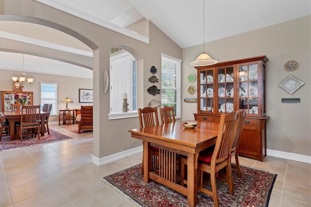 dining area with light tile patterned floors, baseboards, arched walkways, and vaulted ceiling