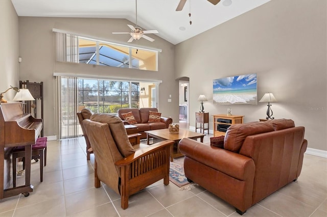 living area with arched walkways, light tile patterned floors, a ceiling fan, high vaulted ceiling, and baseboards