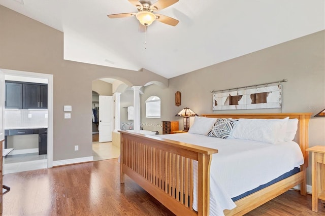 bedroom featuring decorative columns, baseboards, arched walkways, wood finished floors, and vaulted ceiling