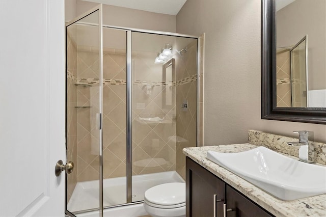 bathroom with a textured wall, a shower stall, toilet, and vanity