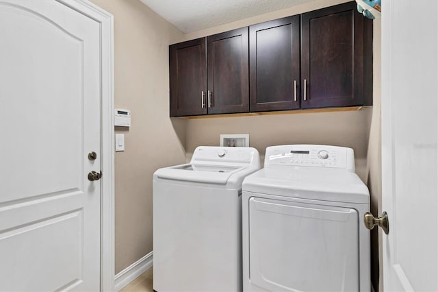 laundry area with a textured ceiling, washing machine and dryer, cabinet space, and baseboards