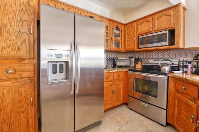 kitchen with light tile patterned floors, stainless steel appliances, decorative backsplash, and brown cabinets