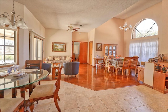 dining area with light tile patterned floors, visible vents, a high ceiling, a textured ceiling, and ceiling fan with notable chandelier