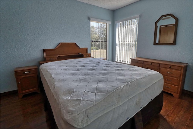 bedroom with a textured ceiling, a textured wall, dark wood-style flooring, and baseboards