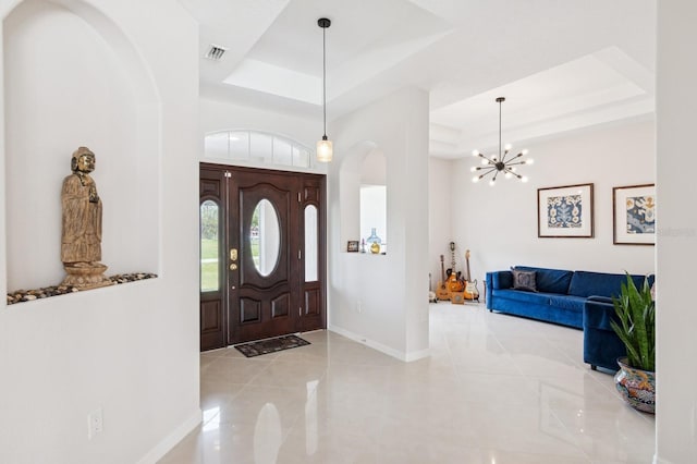 tiled entrance foyer with arched walkways, a raised ceiling, visible vents, an inviting chandelier, and baseboards