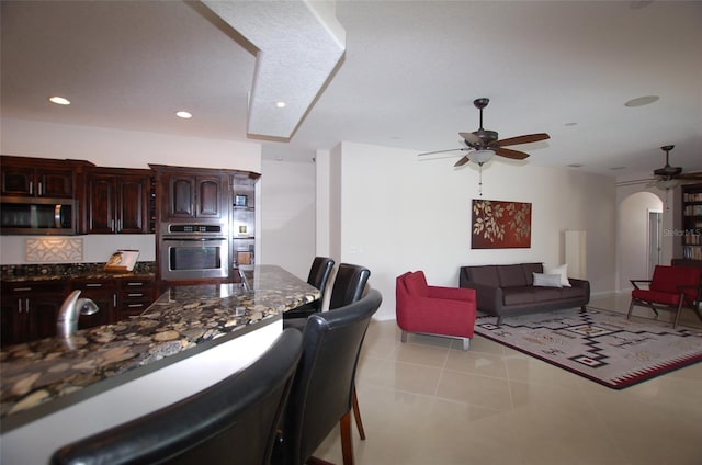 kitchen with arched walkways, recessed lighting, stainless steel appliances, dark stone countertops, and a kitchen bar