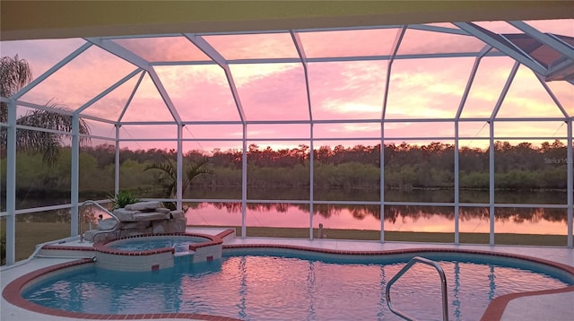 pool at dusk featuring a water view, glass enclosure, a pool with connected hot tub, and a patio