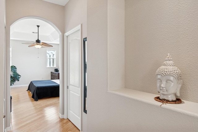 hallway with arched walkways, visible vents, light wood-style flooring, and baseboards