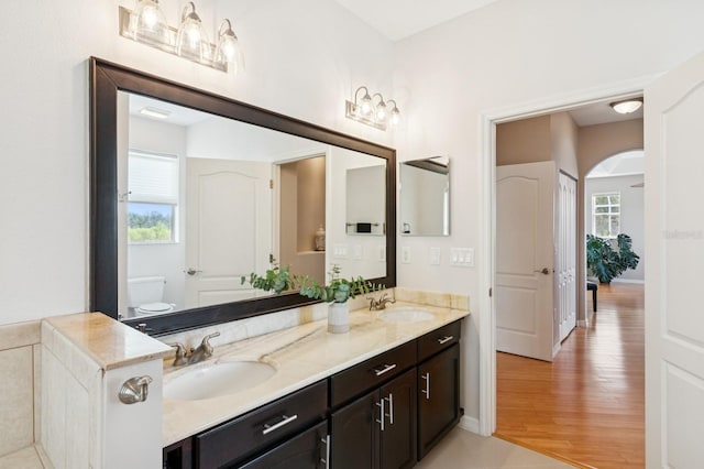 full bath featuring double vanity, toilet, a sink, and wood finished floors