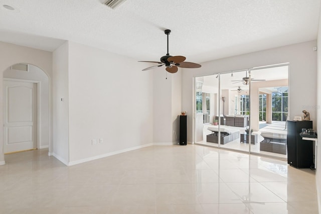 tiled empty room featuring a textured ceiling, arched walkways, visible vents, and baseboards