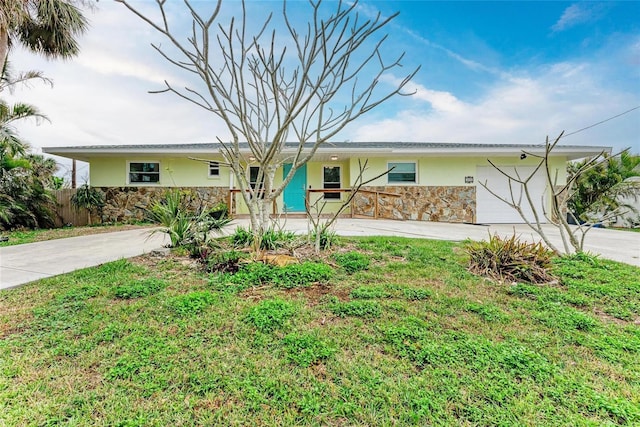 ranch-style house featuring concrete driveway, stone siding, fence, a front lawn, and stucco siding