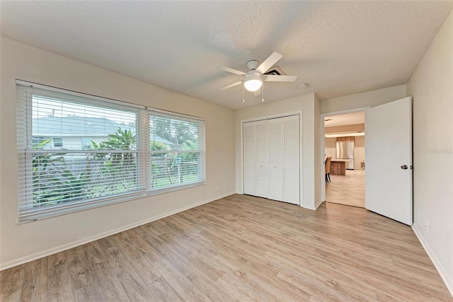 unfurnished bedroom with light wood-type flooring, a closet, a textured ceiling, and baseboards