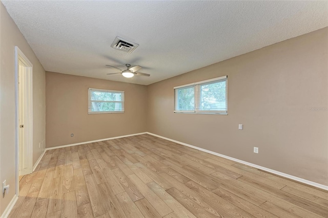 empty room featuring visible vents, light wood-style floors, a ceiling fan, a textured ceiling, and baseboards