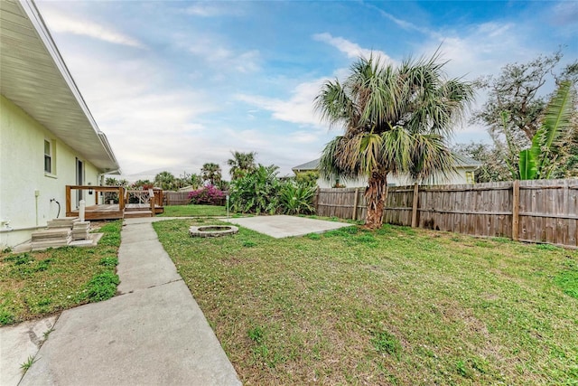 view of yard featuring a fenced backyard, a fire pit, a wooden deck, and a patio