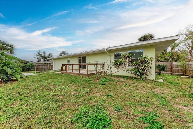 back of property featuring a yard, a fenced backyard, a deck, and stucco siding