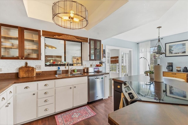 kitchen featuring a sink, dishwasher, dark countertops, a raised ceiling, and glass insert cabinets