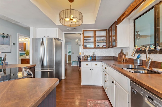 kitchen featuring dark wood finished floors, a raised ceiling, a sink, stainless steel appliances, and backsplash