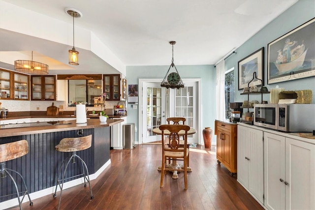 kitchen featuring french doors, stainless steel microwave, glass insert cabinets, dark wood-type flooring, and a kitchen bar