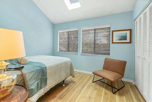 bedroom featuring vaulted ceiling with skylight, a closet, wood finished floors, and baseboards