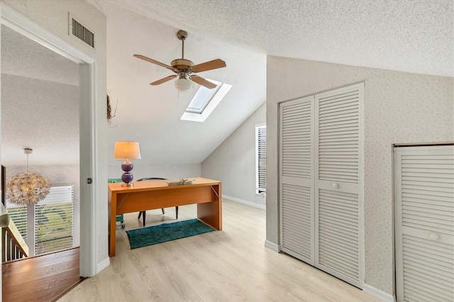 office space with a textured ceiling, vaulted ceiling with skylight, light wood-type flooring, and visible vents