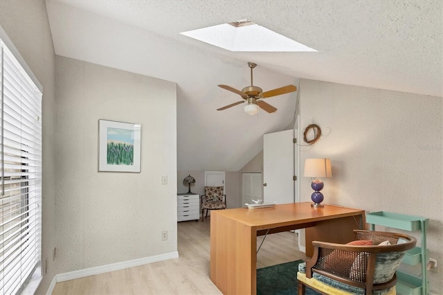 office area featuring light wood-style floors, vaulted ceiling with skylight, plenty of natural light, and a ceiling fan