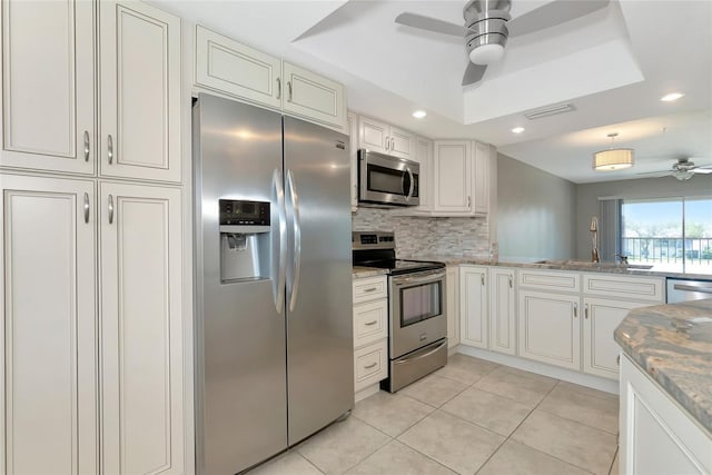 kitchen featuring light tile patterned floors, tasteful backsplash, a ceiling fan, appliances with stainless steel finishes, and a tray ceiling