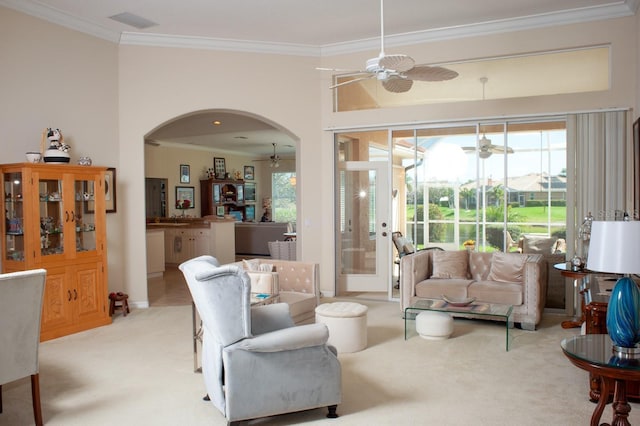 living area featuring ornamental molding, ceiling fan, arched walkways, and light carpet