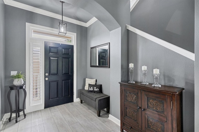 foyer with arched walkways, light wood-style flooring, baseboards, and ornamental molding