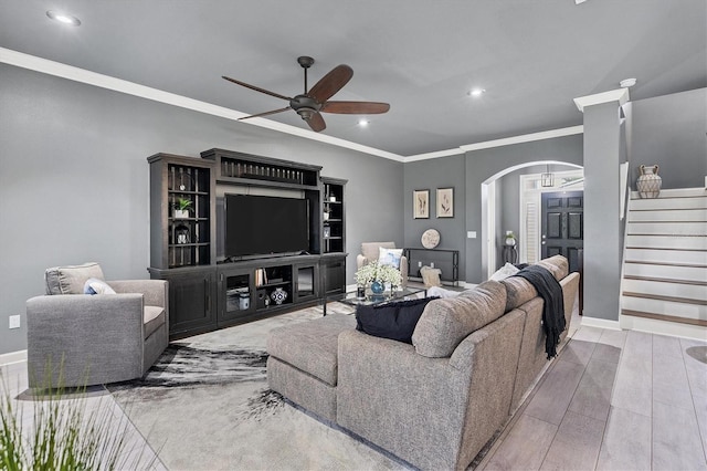 living room featuring stairway, a ceiling fan, wood finished floors, arched walkways, and crown molding