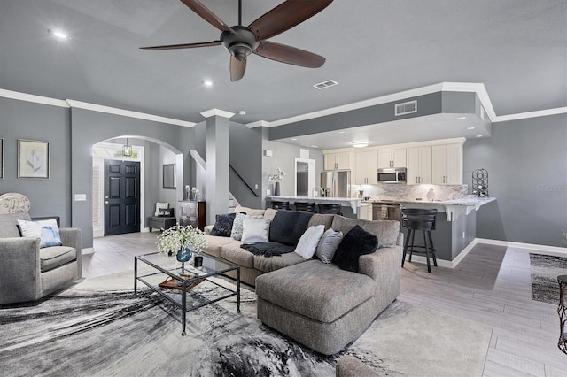 living room featuring arched walkways, visible vents, light wood finished floors, and baseboards