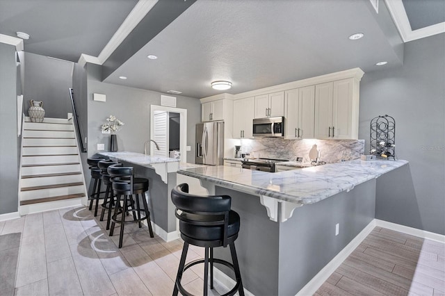 kitchen featuring light stone countertops, wood tiled floor, a peninsula, appliances with stainless steel finishes, and tasteful backsplash