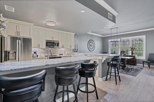 kitchen featuring visible vents, a breakfast bar, appliances with stainless steel finishes, a peninsula, and decorative backsplash