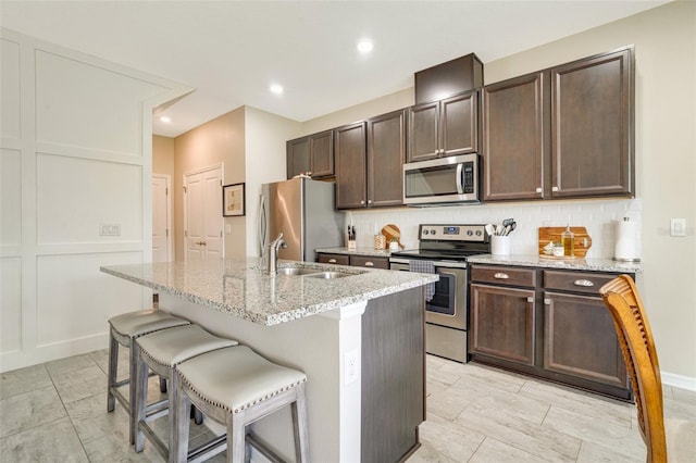 kitchen featuring tasteful backsplash, appliances with stainless steel finishes, a sink, dark brown cabinets, and a kitchen bar